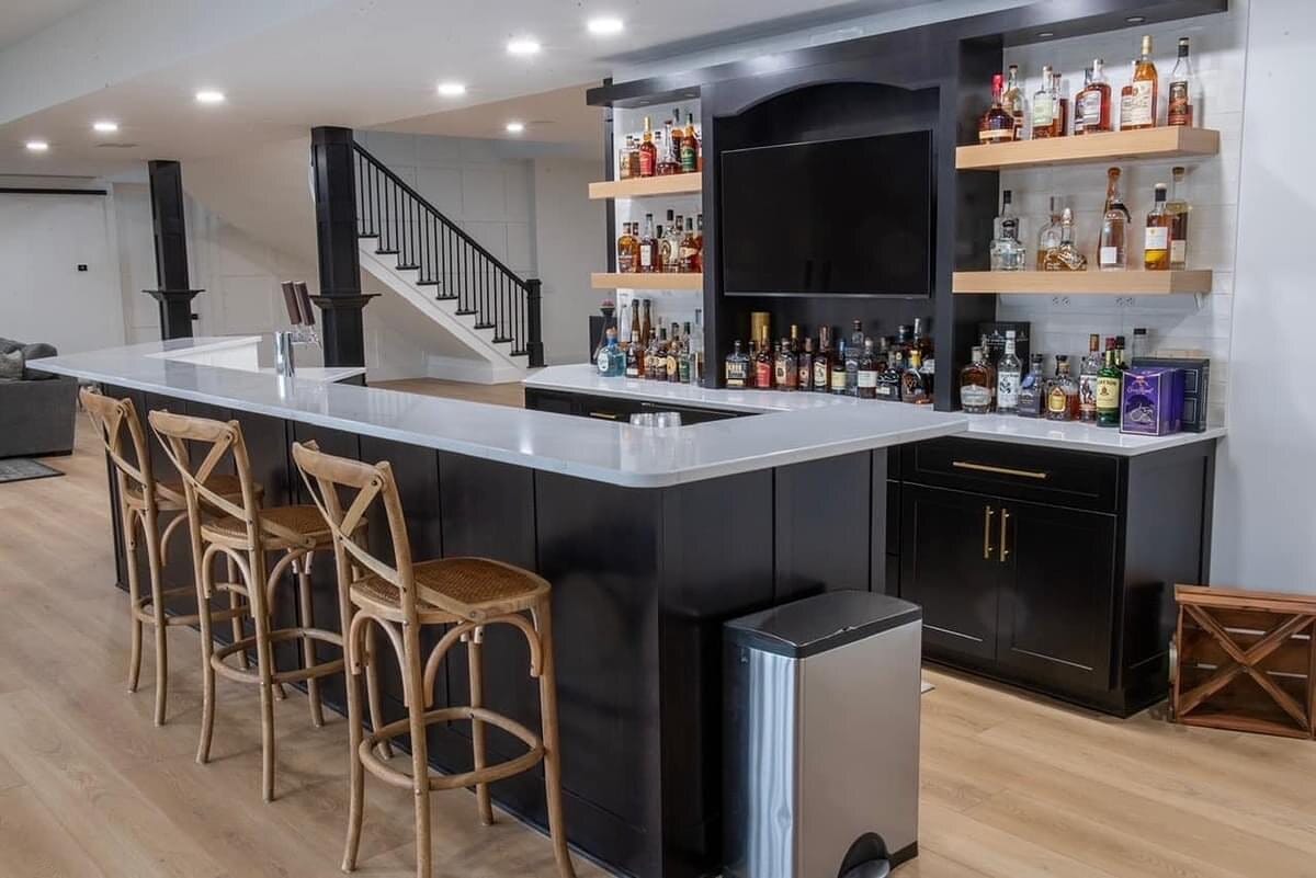 Finished basement bar with dark cabinetry, quartz counters, backlit open shelving, and counter stool seating.