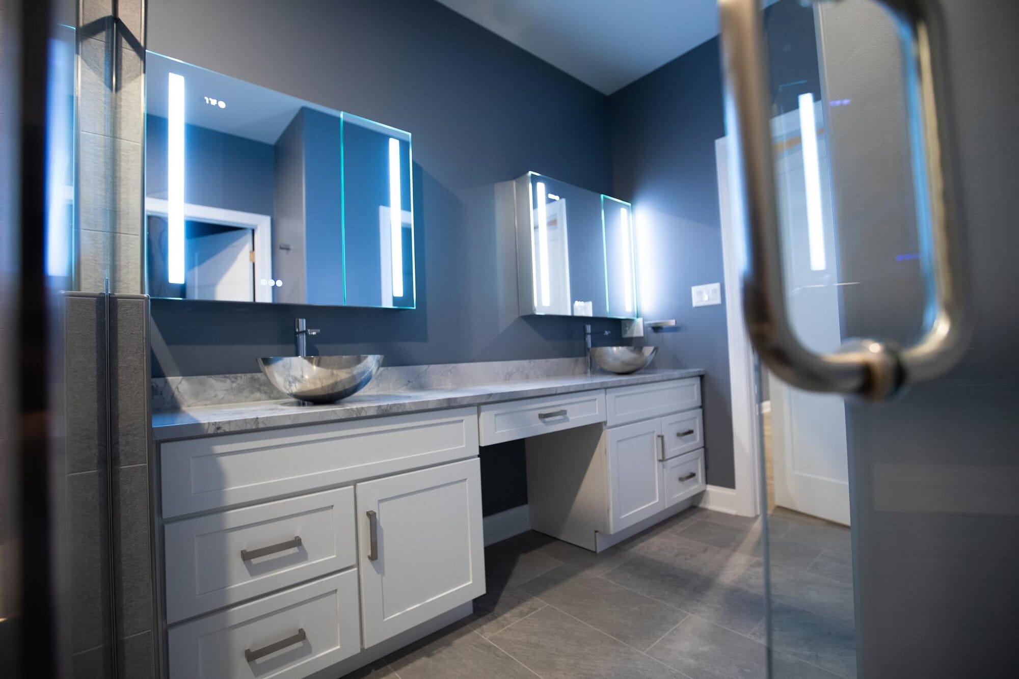 Bathroom vanity run with white cabinetry, granite top, integrated makeup station, and backlit LED mirrors.