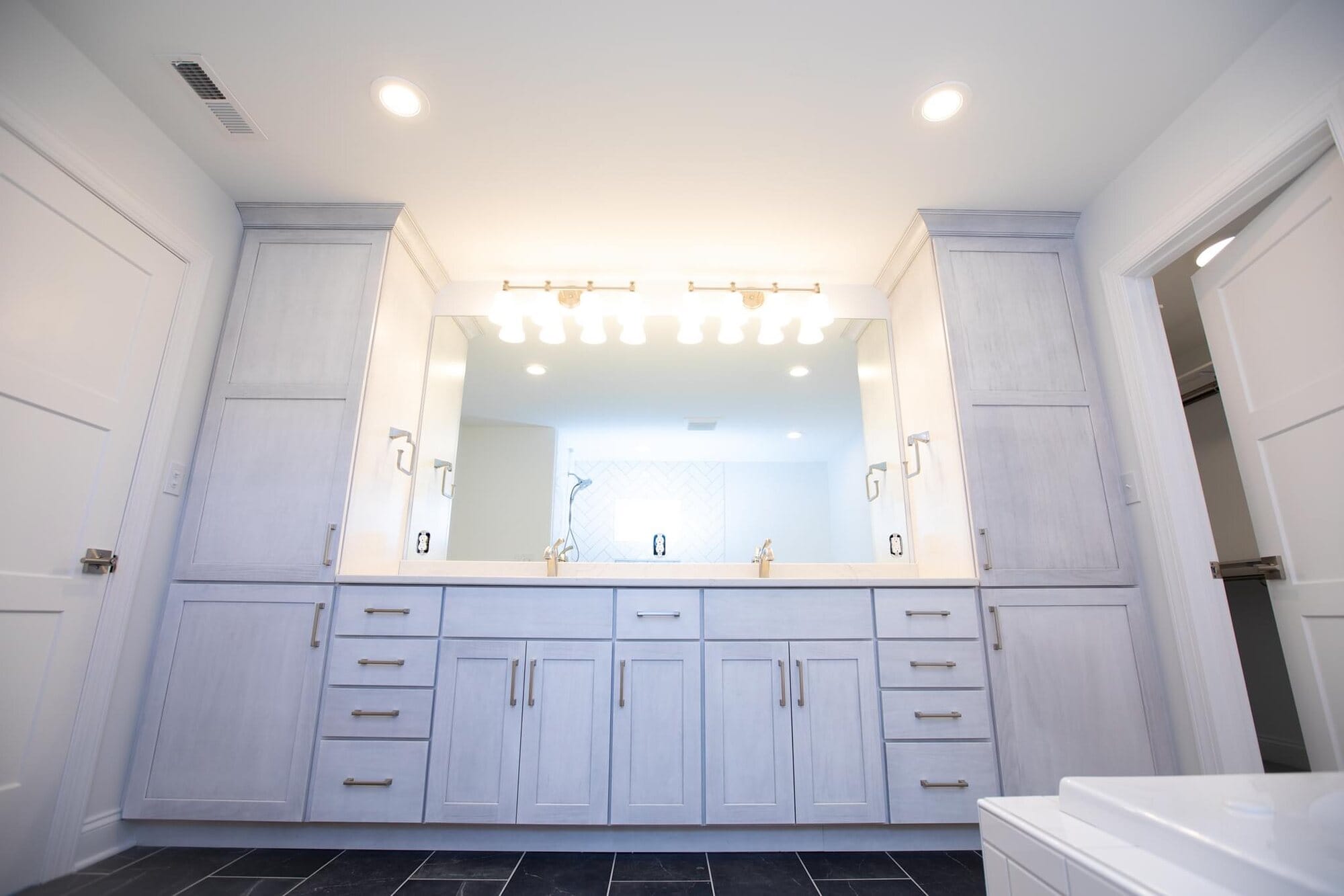 Double bathroom vanity in white cabinetry with a quartz top, large frameless mirror, and multi-globe vanity light bar.