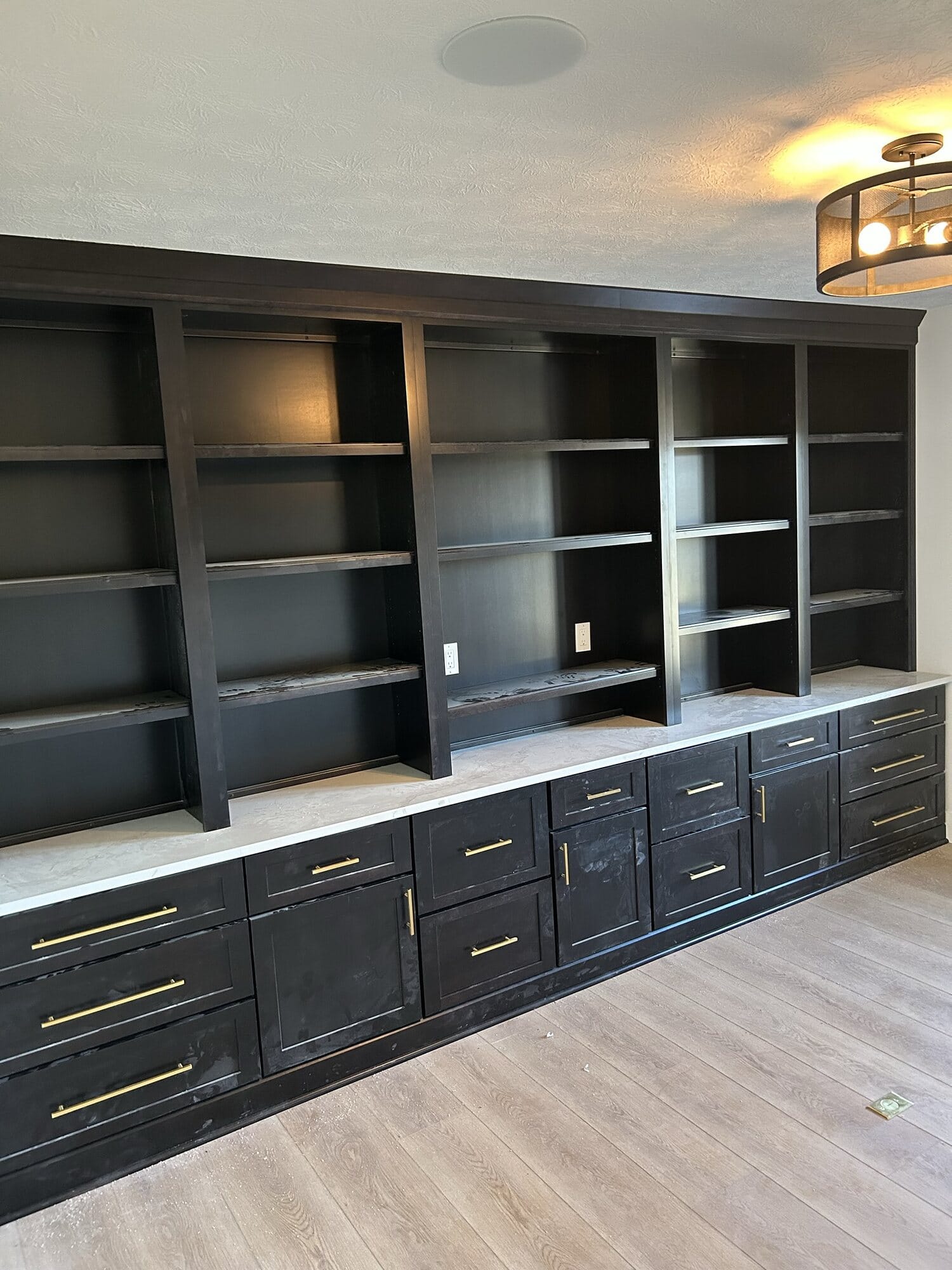 Floor-to-ceiling built-in media wall with black cabinetry, open display shelving, brushed gold hardware, and quartz counter.