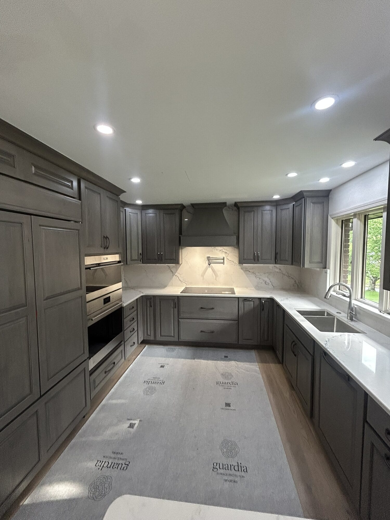 U-shaped kitchen in gray stained cabinetry with double wall ovens, quartz countertops, and a custom vent hood surround.