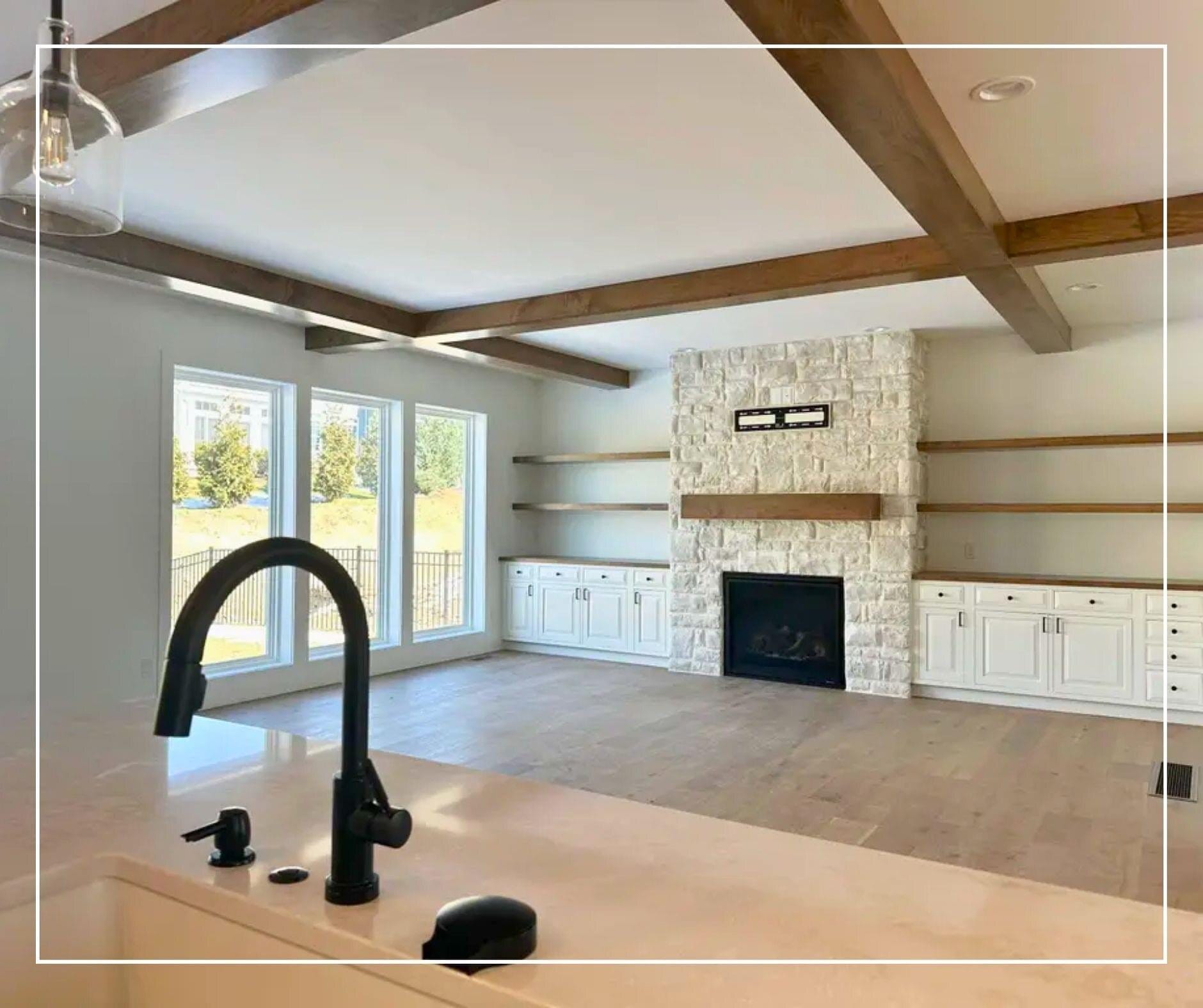 Great room with a stacked stone fireplace, exposed wood beams, floating shelves, and white built-in cabinetry.