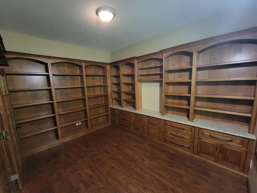 Custom home library built-ins in stained wood with arched open shelving, base cabinets, and a stone countertop ledge.