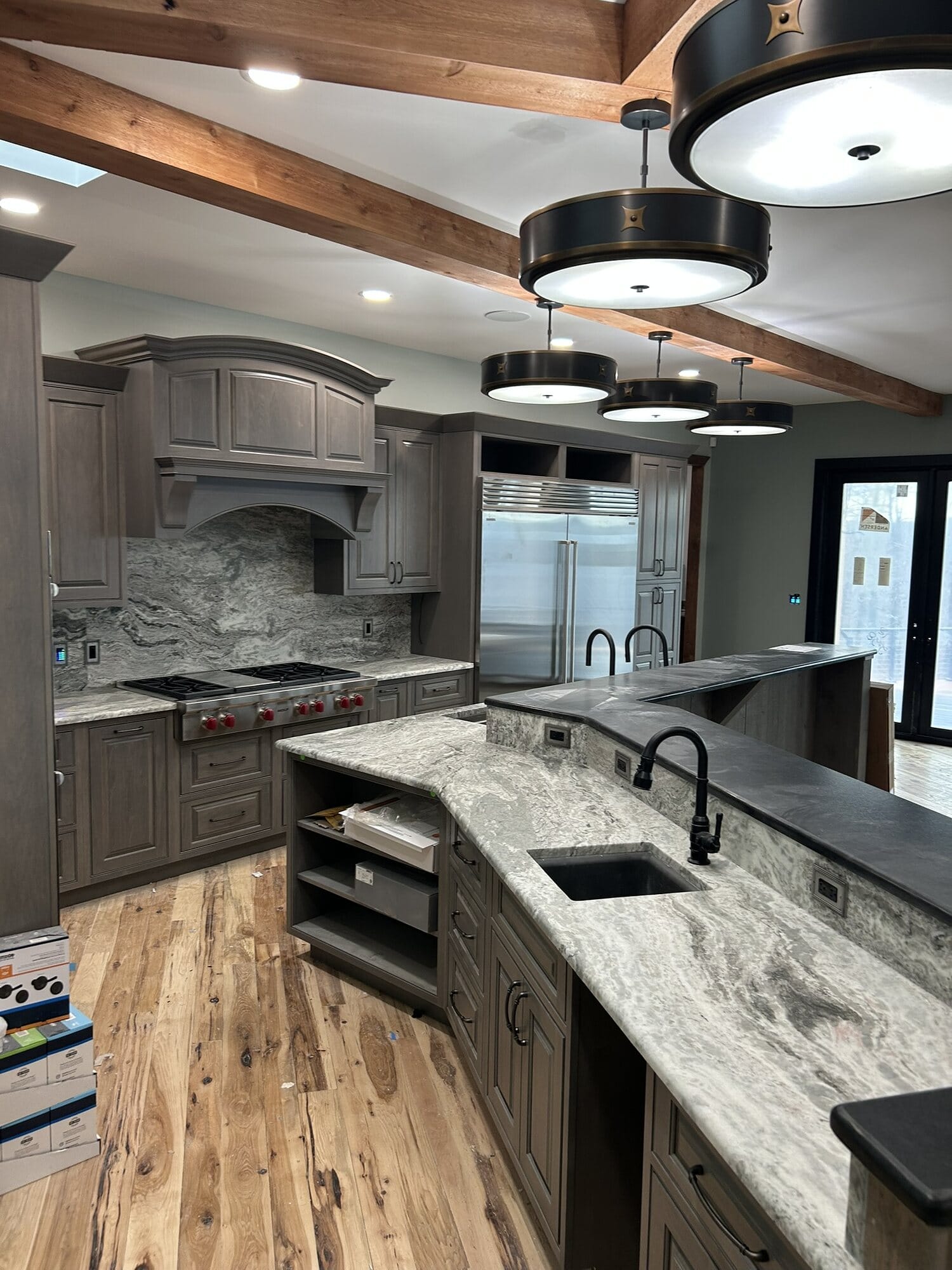 Kitchen with a granite-topped island, custom gray stained hood surround, gas range, and open display shelving.