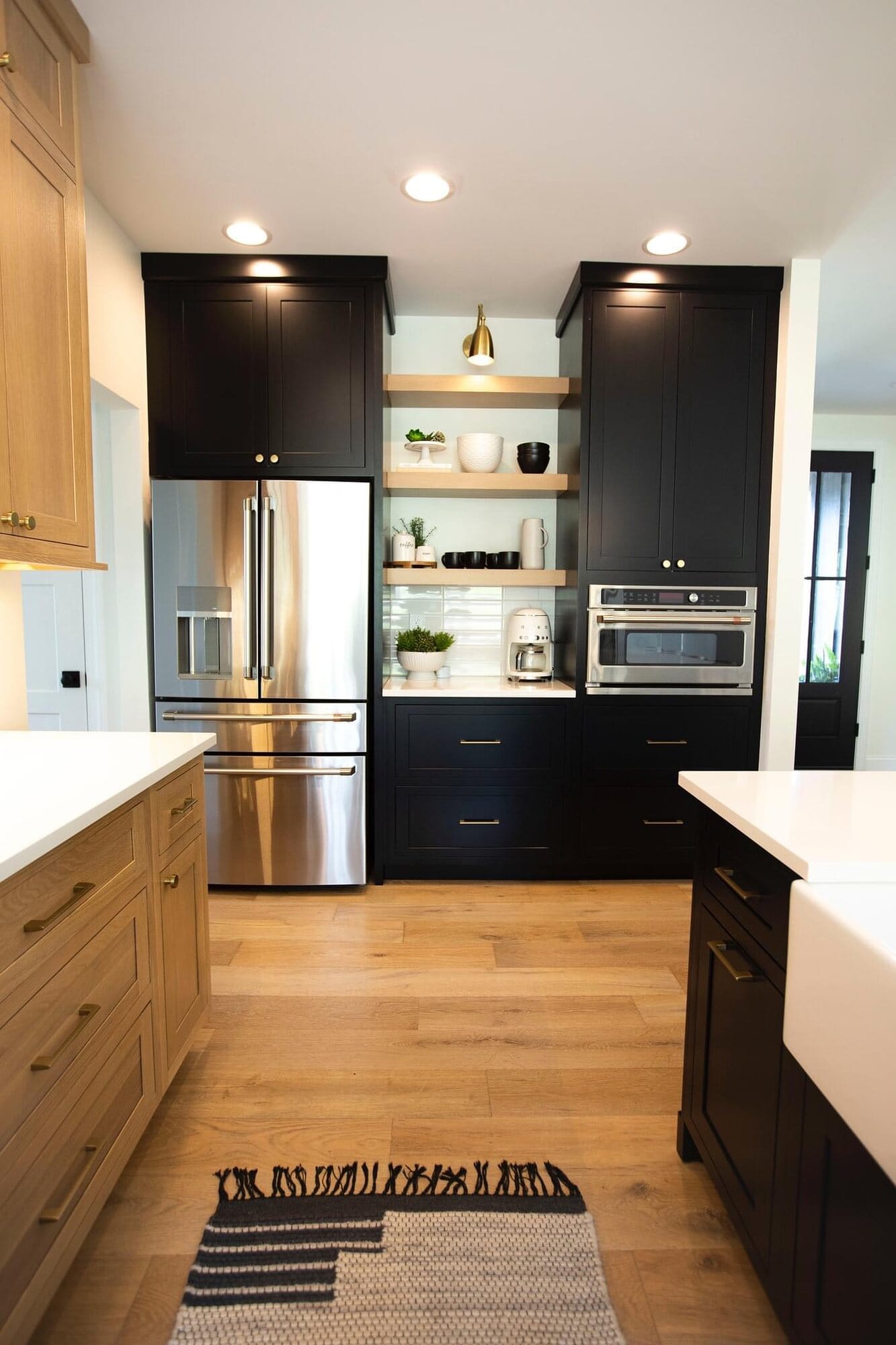 Contemporary kitchen mixing light oak and black cabinetry with brass open shelving, built-in wall oven, and quartz countertops.
