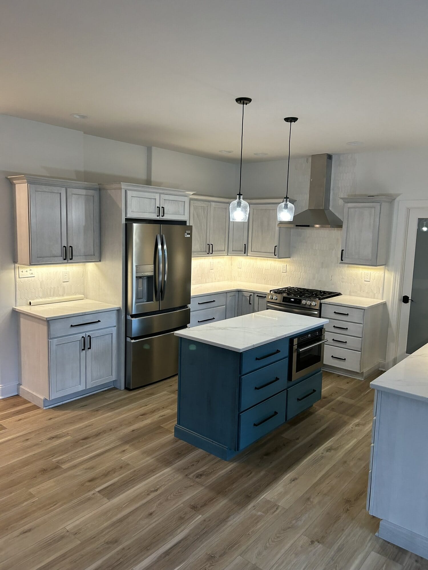 Kitchen with white perimeter cabinetry, a blue painted island, stainless appliances, and wood-look plank flooring.