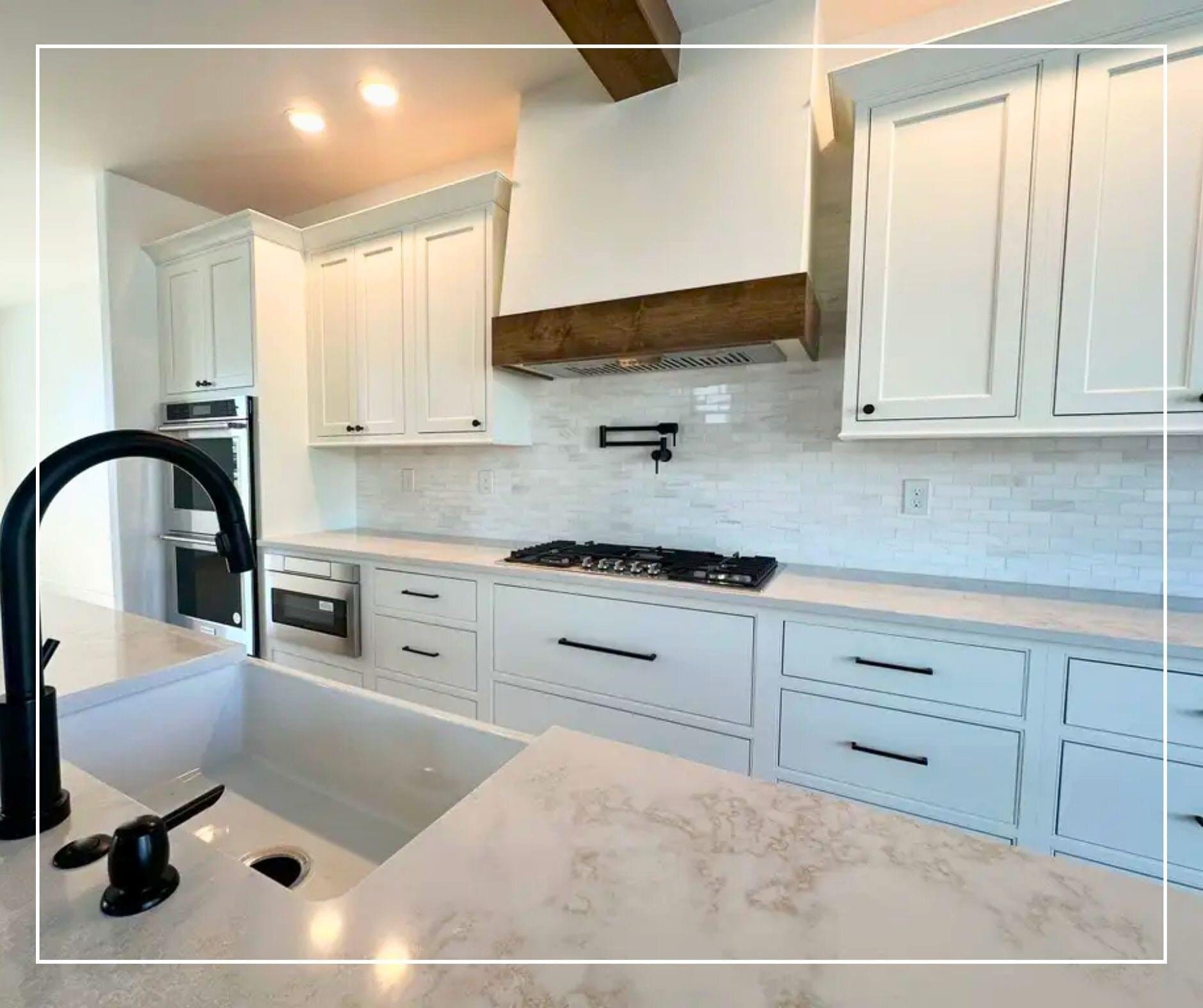 Kitchen with white cabinetry, a stained wood vent hood, marble backsplash, matte black faucet, and quartz countertops.