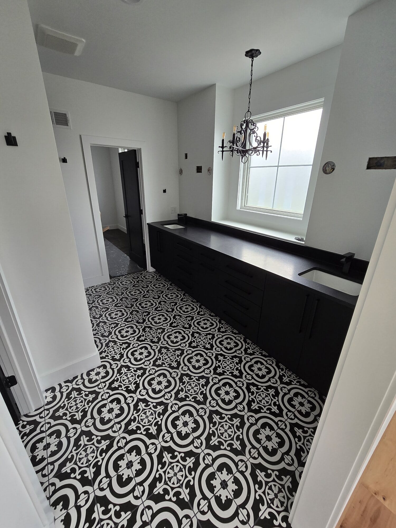 Custom laundry room featuring black shaker cabinetry, a dark countertop with undermount sink, and a black-and-white encaustic patterned tile floor.