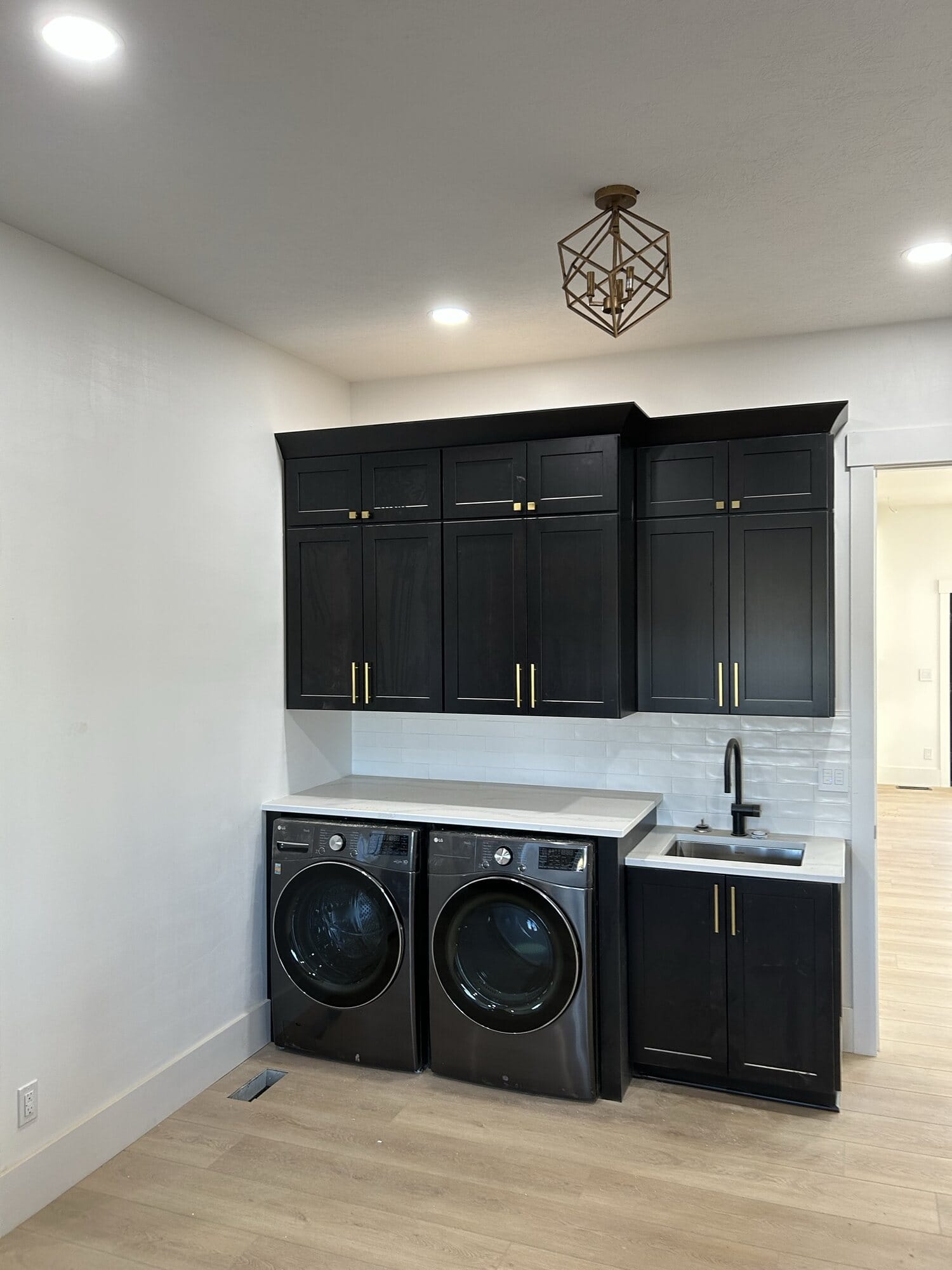 Laundry room with dark painted cabinetry, quartz folding counter, undermount utility sink, and front-load washer and dryer.