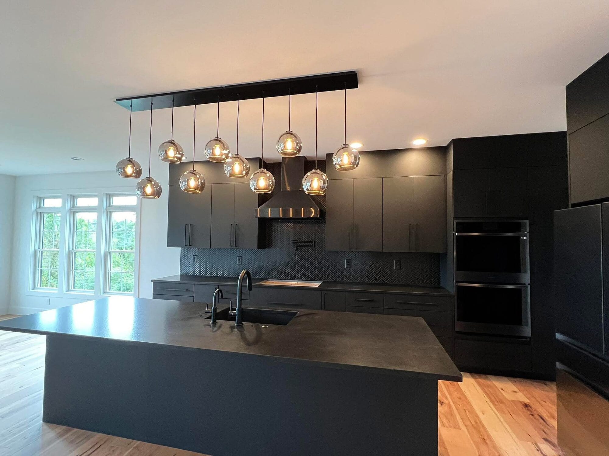 Contemporary kitchen with matte black cabinetry, a black island with waterfall top, and a sculptural glass globe pendant cluster.
