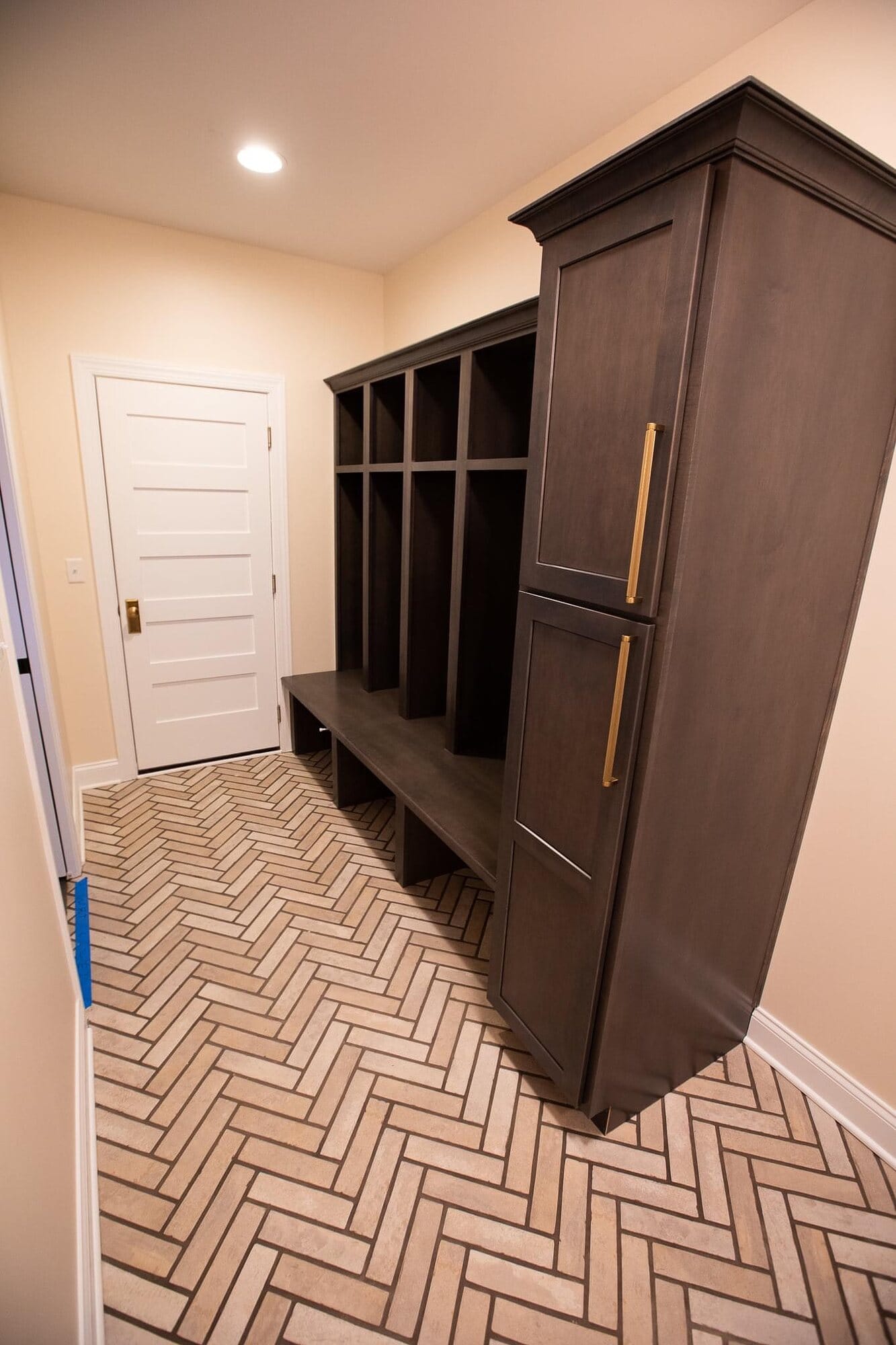 Custom mudroom locker unit in dark stained wood with open cubbies, bench seating, and a herringbone brick-look tile floor.