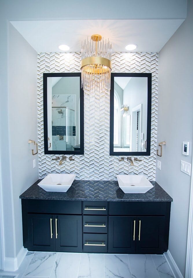 Powder bath featuring a navy floating double vanity, vessel sinks, brushed gold fixtures, chevron tile accent wall, and marble-look flooring.