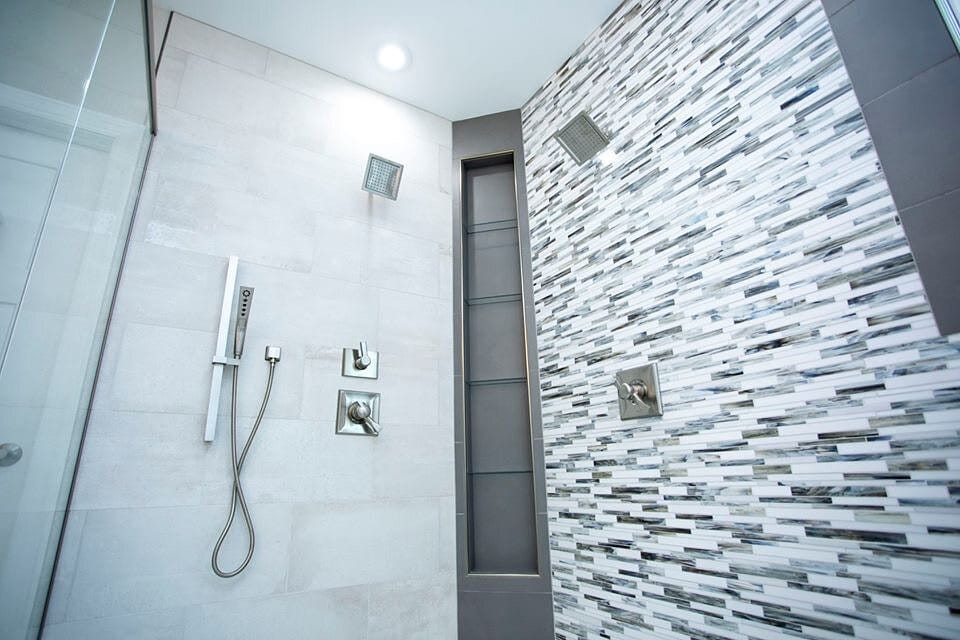 Walk-in shower with a vertical glass mosaic accent wall, large-format tile surround, and a handheld shower fixture.