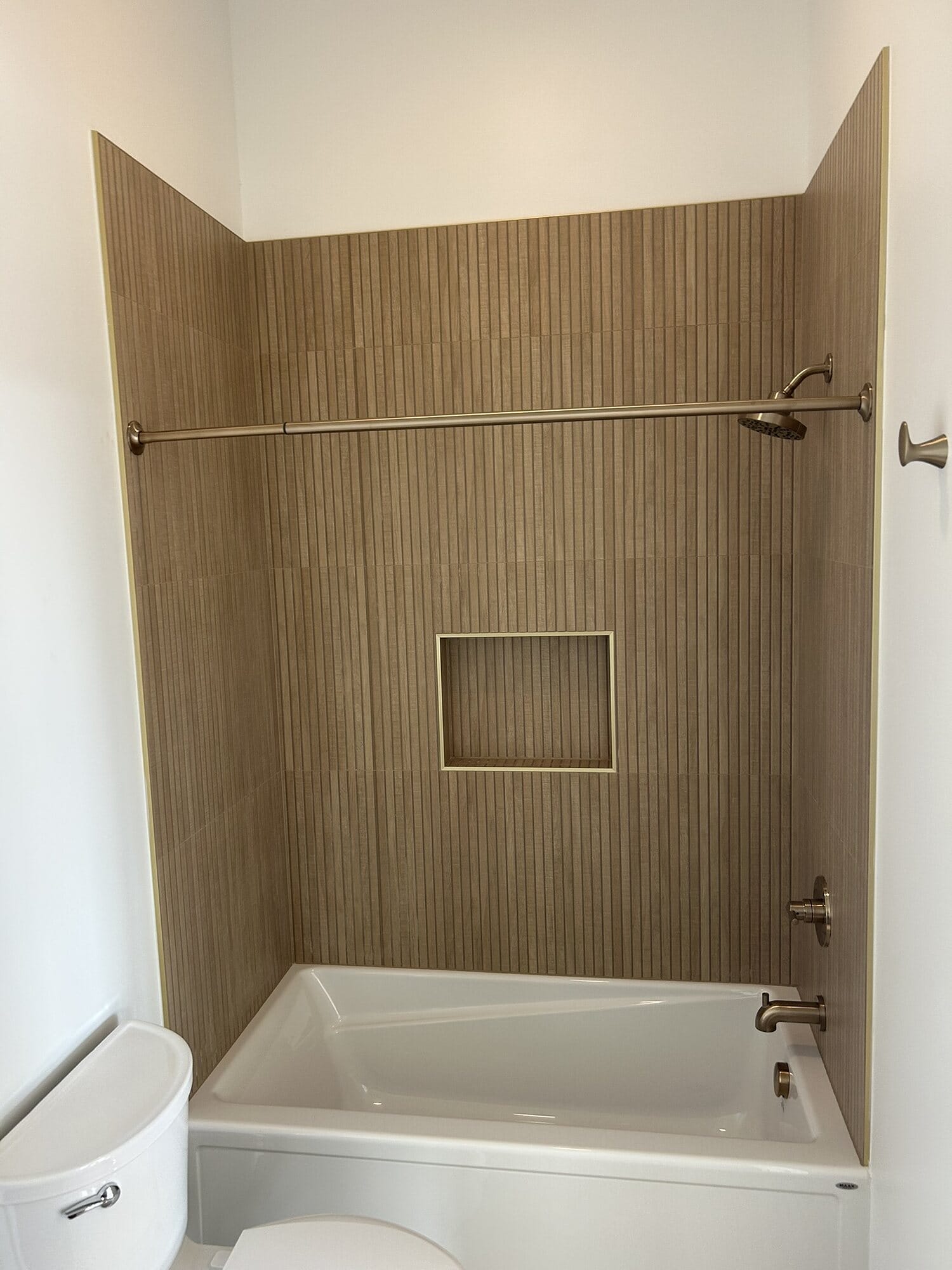 Tub and shower combination with a wood-look tile surround, recessed niche, curved shower rod, and brushed nickel fixtures.