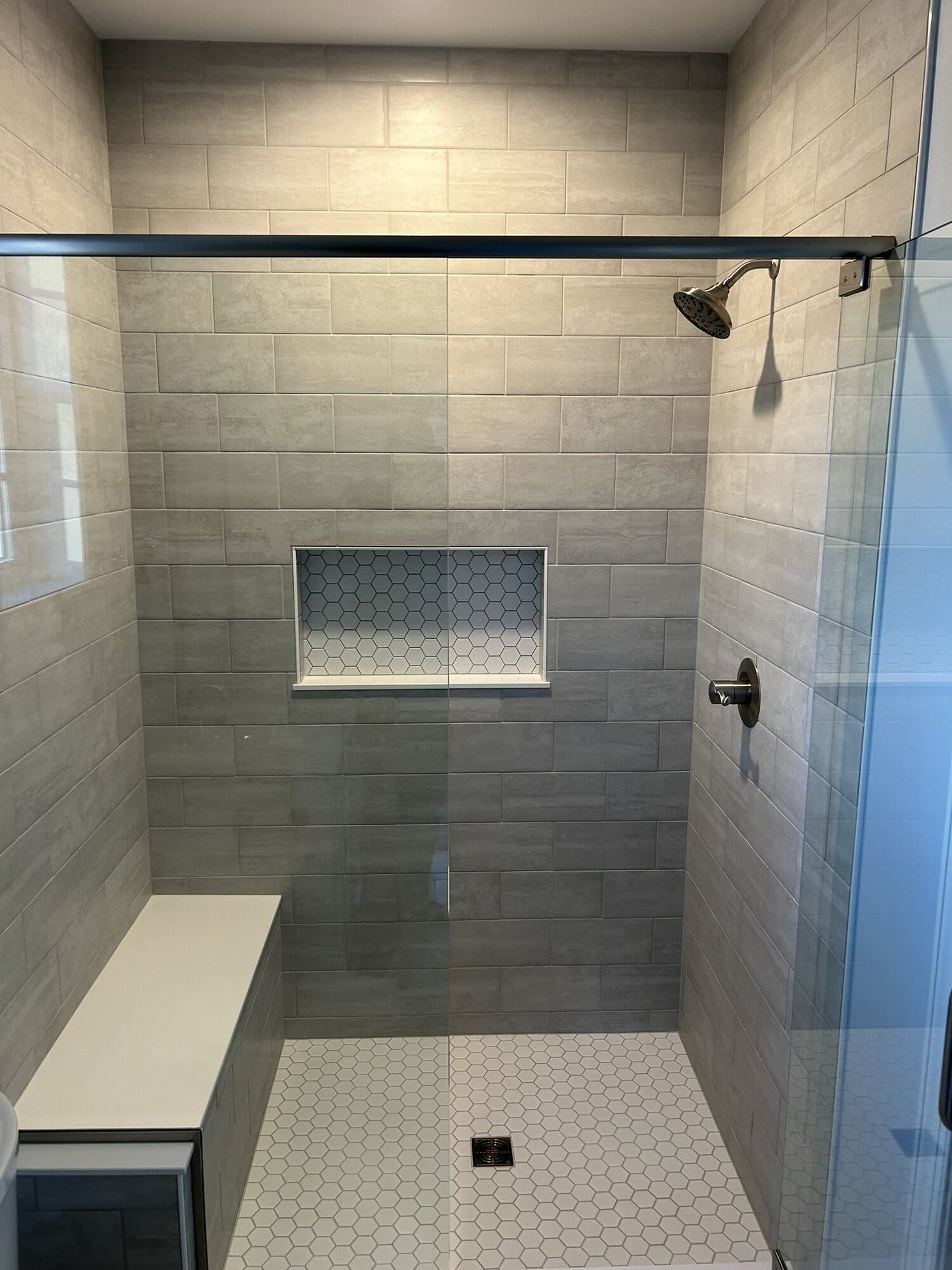 Walk-in shower finished in gray tile with a mosaic floor, built-in bench, accent niche, and glass panel enclosure.