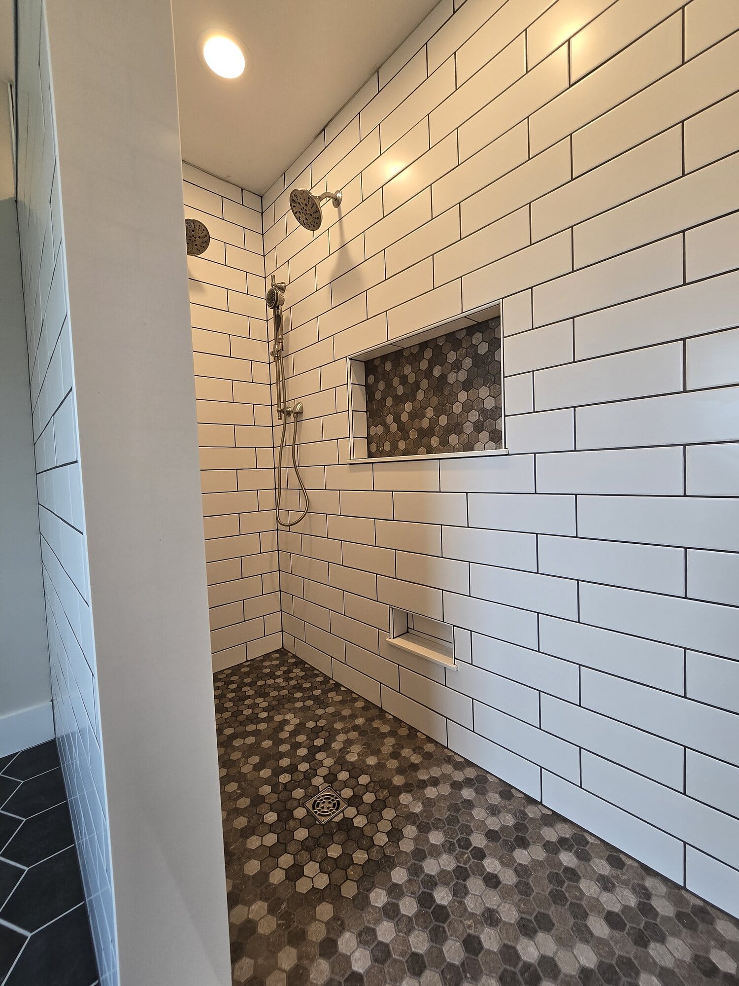 Tiled walk-in shower with white subway tile walls, a built-in niche, matte black fixtures, and a patterned mosaic shower pan.