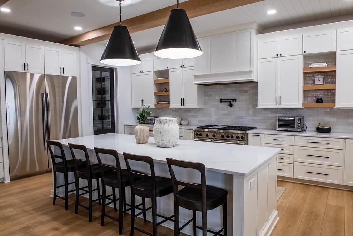 White kitchen with black cone pendants over the island, floating wood shelves, pro-style range, and marble tile backsplash.