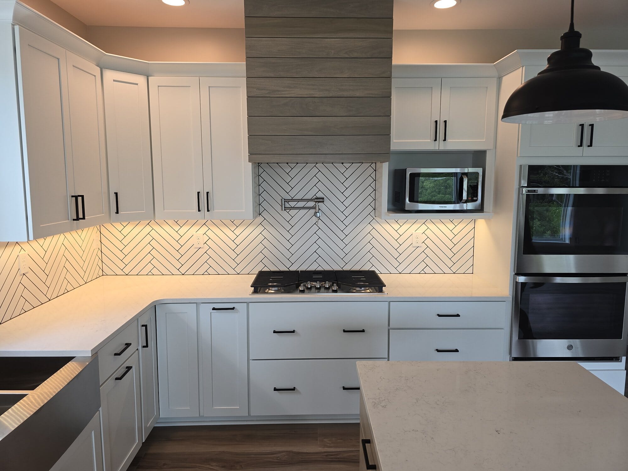 White shaker kitchen with a herringbone tile backsplash, quartz countertops, double wall ovens, and black hardware.